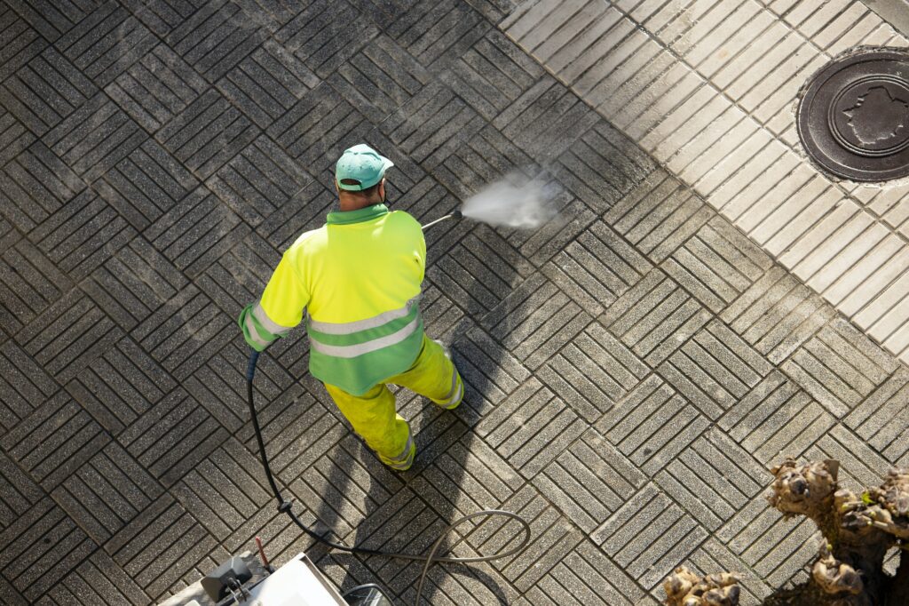 Worker cleaning a street sidewalk with high pressure water jet machine